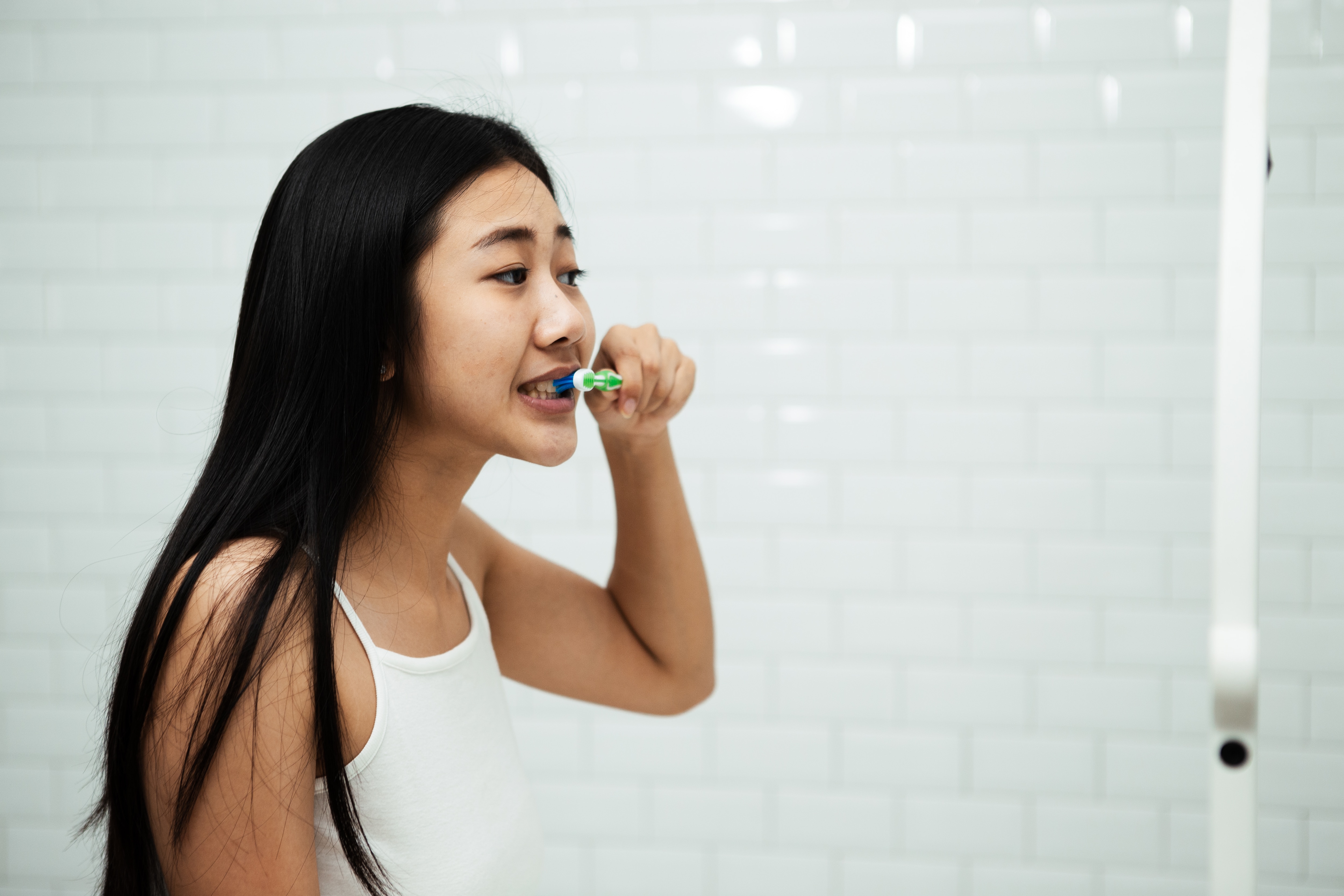 Woman brushing and having thoughts on how to stop gum bleeding while looking in the mirror  